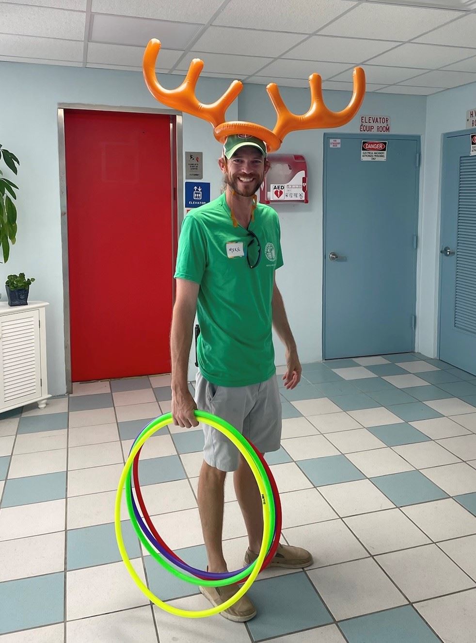 Mike wearing blowup antlers holding rings for kids to toss at his head